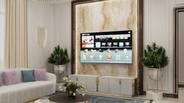 This picture shows an elegant, contemporary living room designed by Antonovich Design. The room has a luxurious, muted palette with white walls, a black and grey marbled floor, and plush beige furniture. There is a fireplace set into a white stone wall, a large glass window with a beautiful view, and a curved sofa sectional in the center of the room. An abstract painting hangs over the sofa, and on either side are two black armchairs with light gray upholstery. The room also features a sleek black coffee table and a modern, textured rug.