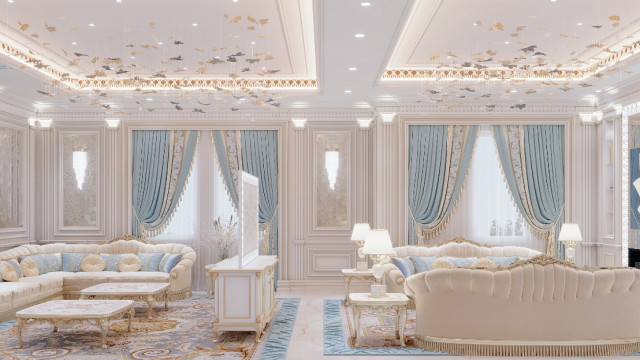 This picture shows an ornate sitting area with a modern design. The room features a luxurious, tufted ivory sofa with two matching armchairs, placed on a plush cream-colored area rug. There is a round, lucite coffee table in the center of the seating area and a mirrored side table against one wall. A statement chandelier hangs from the ceiling, and other modern elements such as an abstract art piece and patterned pillows add to the room's contemporary feel.