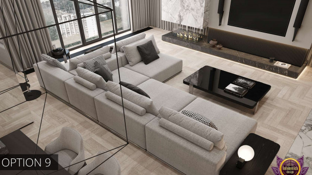 This picture shows a modern and luxurious living room. It has a white area rug, two black sofas, two light grey armchairs, a round coffee table with a glass top, several plants, and a fireplace in the corner.