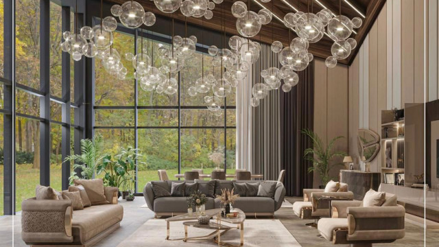 This is a modern-style living room designed by Antonovich Design. It has black marble walls and a blank panel in the center. On either side of the panel are two walls with shelving units that hold a variety of decorative items such as books, frames, and sculptures. The flooring is a light colored hardwood and there is a white area rug. At the center of the room is a large white leather sofa accompanied by matching ottomans. There is also a black and white armchair and a light blue chaise lounge.