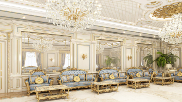 This picture shows a luxurious living room with high ceilings and a grand statement staircase. The walls are painted in a white color and adorned with plenty of artwork. There is a gray velvet sofa with several throw pillows, a coffee table and several side tables filled with decorative items including vases, books, and small sculptures. On the two walls facing the sofa are two tall glass doors leading out to a balcony that overlooks the city skyline.