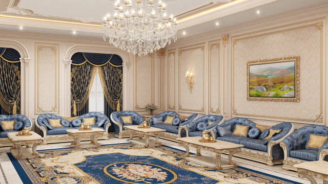 This picture shows a luxurious, spacious living room with beige furniture and accents. The large L-shaped cream sofa faces a white stone fireplace and an ornate crystal chandelier hangs above it. The walls are decorated with elegant wallpaper and the floor is carpeted in a light beige color. There is also a small round glass coffee table in front of the sofa and two white armchairs flanking the fireplace.