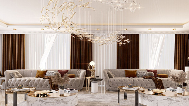 This picture shows a modern living room interior design. It features a cream-colored sofa with two gold velvet ottomans in front of it, a round glass coffee table, two gray chairs with patterned upholstery flanking the sofa, and a white marble floor. The walls are painted an off-white color and feature decorative panels. A large chandelier hangs from the ceiling and soft lighting from wall sconces add to the overall ambiance of the room.
