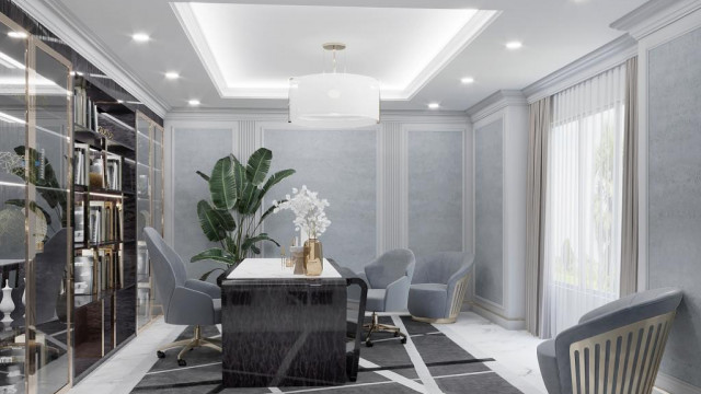 This picture shows an interior design of a living room with a modern and luxurious style. The room features grey walls, dark hardwood flooring, and a sectional couch in white leather upholstery. The room is lit by a modern chandelier, and there is a square coffee table surrounded by white leather armchairs with silver legs. A beige rug and several abstract art pieces decorate the space, creating a sophisticated and stylish look.