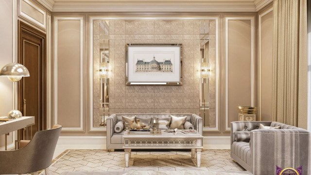 This picture shows a luxurious modern living room designed by the interior design firm Antonovich Design. It features an ivory leather sectional sofa, a glass coffee table with gold accents, a marble fireplace, and a large flat-screen television mounted on the wall. The room is decorated with plush accent pillows, and there are two sets of gold curtains framing the windows. There is also an elegant chandelier hanging from the ceiling, adding a touch of glamour to the room.