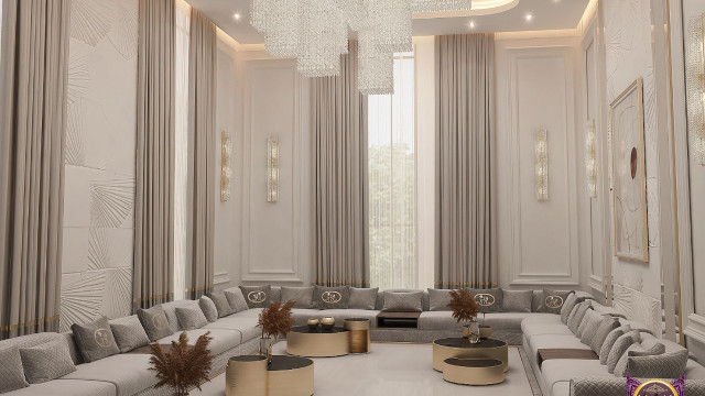 This picture shows a luxurious modern living room with a large, white sectional sofa and a dark wooden accent table in the center. The walls are a warm gray color, and there is a built-in fireplace on one wall. The ceiling is vaulted and there is a large crystal chandelier hanging from it. There are also two glass doors leading to an outdoor terrace. The floor is tiled in a light beige color, and there is a rug in the seating area for added warmth.