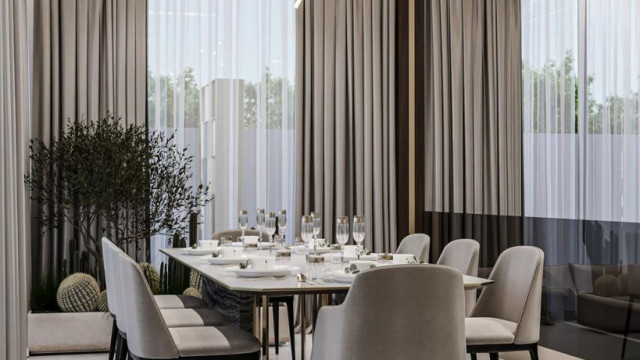 An outdoor dining area featuring a long table with chairs, surrounded by lush green vegetation.