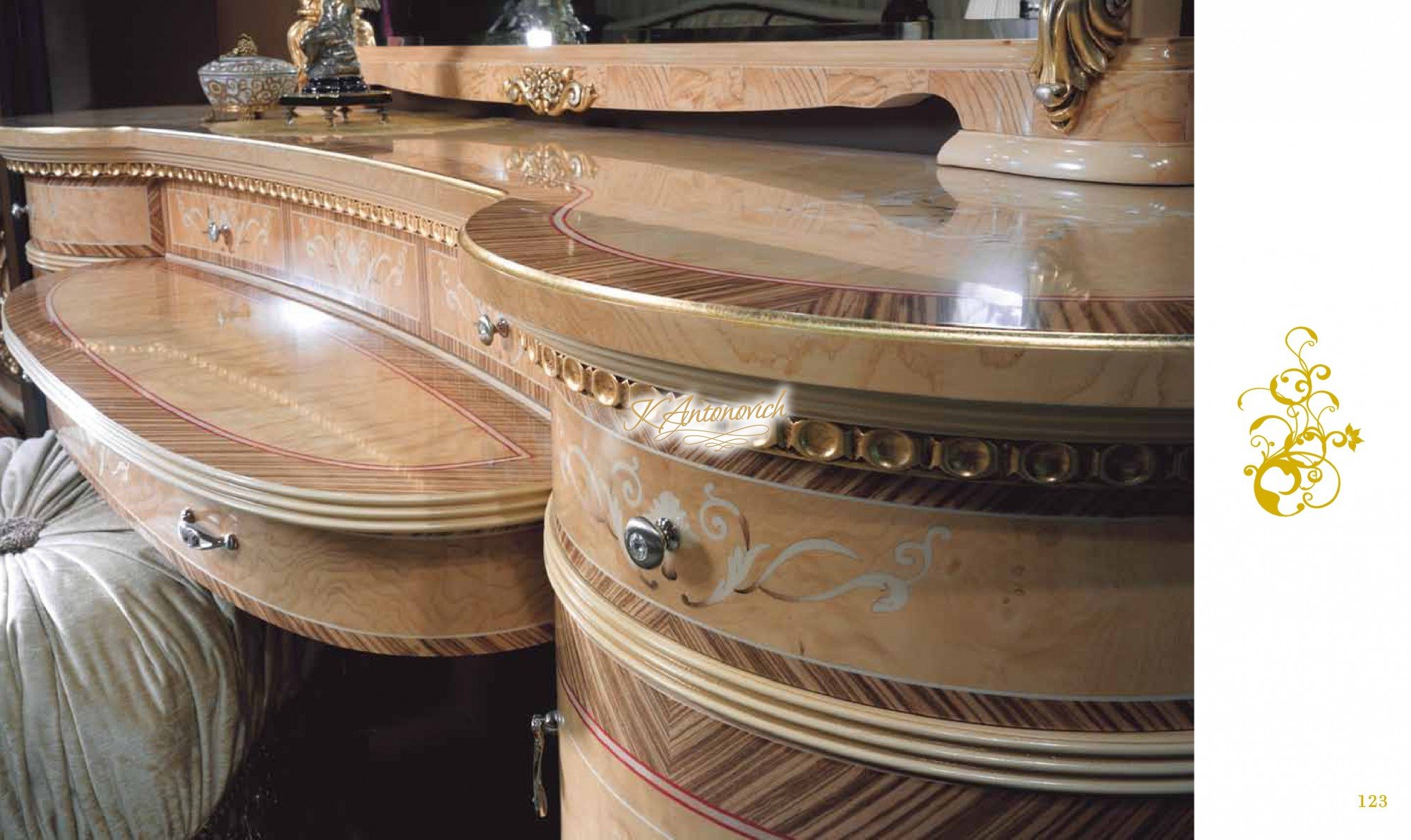 The picture depicts a small, wooden box with a large handle on top. The top of the box has a slanted lid with an intricate design of two birds and floral scrollwork. There is a brass latch at the front of the box and several decorative nails at the sides and corners. The box appears to be made of light-colored wood and has a slightly aged or weathered look.