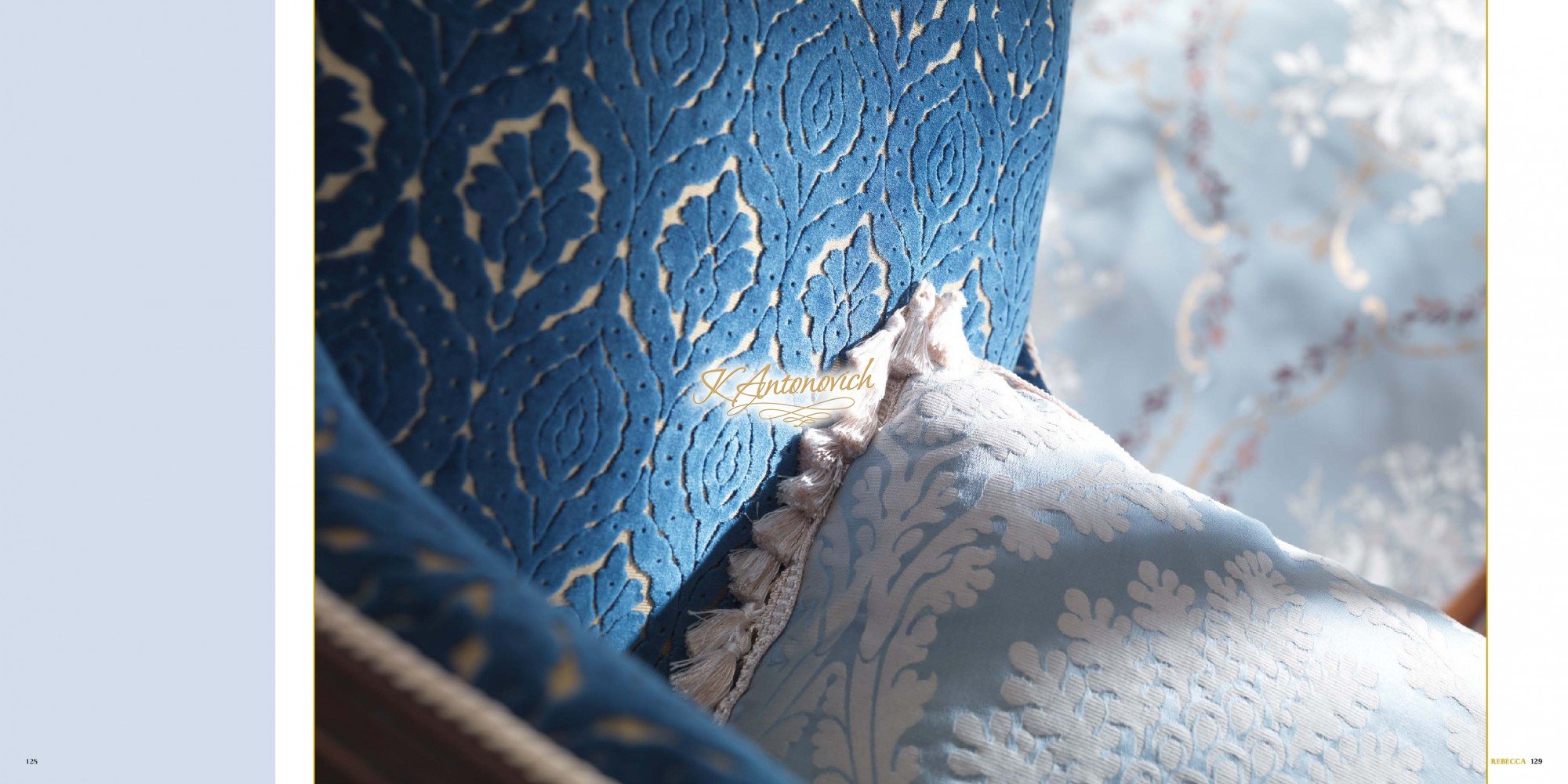 This picture is of a small, white kitten perched on the arm of a gray loveseat. The kitten is curled up with its head resting on its paws, looking off into the distance. Its eyes are closed, suggesting that it may be sleeping and dreaming.