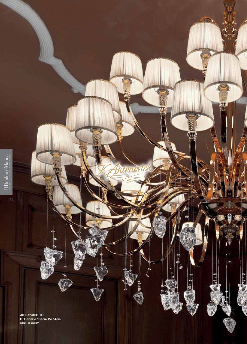 This picture shows the interior of a luxury dining room. The room is decorated in an ornate, elegant style with a grand chandelier and wall sconces adding extra lighting throughout the space. There is a large, round dining table in the center of the room surrounded by chairs upholstered in white fabric. The walls and flooring feature classic white marble and a patterned beige rug beneath the table adds a touch of warmth and texture to the design.