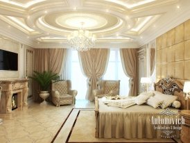 This picture is showing a luxury bedroom designed by Antonovich Design in Abu Dhabi. It features a statement ceiling with intricate details and a modern white hanging lamp. The walls are covered in a textured dark grey wallpaper, and the floor has a plush gray rug. On one side of the room there is a large bed with light gray bedding, and on the other side is a stylish table and chairs set. There is also a window with tall curtains, and a standing mirror near the entrance.