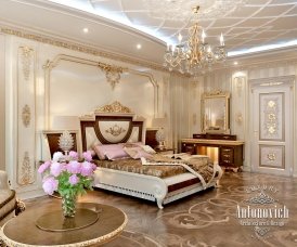 This picture shows a luxurious interior design with a stunning wooden armchair in the foreground. The armchair is a unique velvet upholstery piece with tufted detailing and gold accents. The walls of the room are painted a light shade of blue, and intricate crystal chandeliers adorn the ceiling. There is also a large window with beautiful white shutters and curtains, allowing natural light to flood into the room.