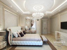 This picture shows a luxurious living room with a modern design. The room is decorated with white furniture, light wood flooring, a beige area rug and matching sofas. The walls are painted in a light beige color, while the ceiling has recessed lighting to provide a warm ambience. There is a large silver chandelier hanging from the ceiling and a crystal wall sconce on the wall. The overall design has a modern touch with classic pieces of furniture, creating an elegant atmosphere.