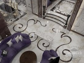 This picture is showing an elegant staircase featuring intricate patterns. The staircase is made of marble and gold, with stairs that curve upward towards the top. The walls feature tiled designs in white and yellow, and the railing has gold detailing that branches off at the top. Additionally, there are two large chandeliers at the bottom of the staircase, adding to the luxurious feel of the space.