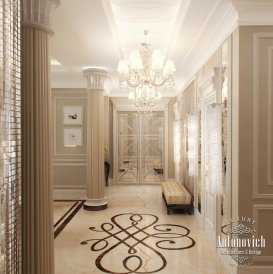 The picture shows a modern luxury bedroom design. The room features light beige walls and carpet, with a textured beige wallpaper accent wall. The center of the room is dominated by a luxurious four poster bed with white and gold detailing. On either side of the bed are floor-to-ceiling wardrobes with contrasting black frames. The bed is dressed with a patterned white and gold throw, and the room is decorated with a variety of wall sconces and art pieces. The room is finished off with a white and gold velvet armchair, adding a touch of elegance