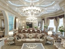 This picture shows a luxurious living room with elaborate marble flooring, large white velvet sofas, and a unique light fixture in the center of the ceiling. A sophisticated chandelier hangs from the ceiling, surrounded by two large wall mirrors. A plush white rug adorns the floor and a glass-top coffee table provides a centerpiece for the room. The walls are decorated with framed paintings, giving the room a warm and inviting atmosphere.