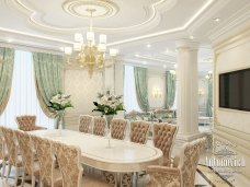 This picture shows a luxurious modern dining room with a gray wall and white wood paneling. The room features a round dining table surrounded by comfortable white chairs with golden accents. There is an elegant chandelier in the center of the ceiling, providing bright light for the room. On the side, there is a floor-to-ceiling window encased in golden frame, letting natural light in. The dark marble flooring, accompanied by a white carpet, completes the sophisticated look of the space.
