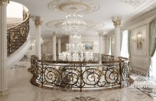 This picture shows a luxurious and modern staircase made from white marble and black metal. The stairs are sweeping, with two curved steps leading up to the next level. The handrails are made of polished chrome and have an elegant design. The walls around the staircase have a stunning patterned wallpaper, and there is an ornate chandelier hanging from the ceiling.