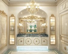 The picture shows an exquisite luxurious bathroom with a large shower area. The overall design is modern and elegant, with walls covered in marble which contrasts with the white vanity and jars of beauty products. There is an open window that provides lots of natural light, as well as two gold-framed mirrors above the wash basins. A small wooden stool is placed in front of the vanity, and there is a built-in shelf above the toilet where towels and toiletries can be stored.