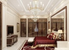 This picture shows a luxury bedroom in a modern home. It features a large king size bed with a white tufted headboard, two nightstands on either side of the bed with lamps, a white tufted bench at the foot of the bed, and a plush white carpet that covers the floor. The walls are painted a light blue color, and there is a large window that brings in lots of natural light. The room also features modern decor, like a large painting hung over the bed, and a vase of flowers on one of the nightstands.