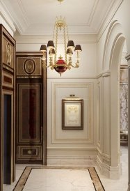 The picture shows a grand, luxurious interior design of a formal living room. The room features deep navy blue walls and plush white furniture, as well as elaborate ceiling decorations, detailed carpets, and a central crystal chandelier. Ornate paintings and sculptures provide a unique touch and add to the luxurious ambiance.