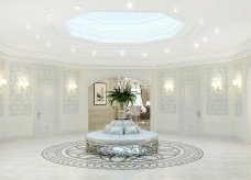 The picture is of an elegance and stylishly designed living room. The room features an intricate ceiling design with elaborate chandelier, ornate golden and silver trimmings, a statement wall with an abstract wallpaper, a white marble floor and a grey sofa set with a round center table. It also includes a two-tier coffee table, gold decor pieces, and various decorative plants.