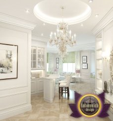 Modern white living room with luxurious details, fitted with grey and yellow pillows and a glamorous chandelier to illuminate the space.