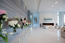 This picture shows a luxurious and elegant living room designed in a modern style. The walls are white with an accent wall in a light gray color. The furniture is mainly neutral with different shades of beige, brown and cream. There is a comfortable leather sofa, coffee table and several armchairs. The floor is dark wood, giving the room a warm and inviting atmosphere.