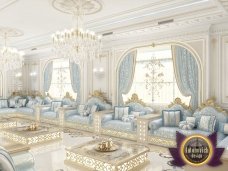 This picture shows a luxury interior design featuring golden accents on the walls and floor. The furnishings include an elegant sofa, a small armchair, a round coffee table, a few side tables, and a large armoire. A golden lighting fixture hangs from the ceiling, while several large windows let in plenty of natural light. A patterned rug covers the marble floor, creating a warm and inviting atmosphere.