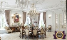 This picture shows an elegant room with a luxurious lighting system. The space features marble flooring, a black crystal chandelier, and long velvet drapes at the entrance. The walls are decorated with golden details and a large mirror. The furniture includes two dark velvet sofas, two wooden coffee tables, and a contemporary armchair with a golden frame.