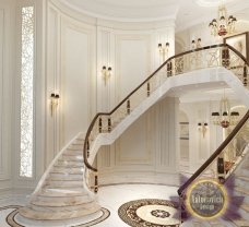 This picture shows a lavish and luxurious interior design. It features an extravagant gold and marble staircase with elaborate details and a large crystal chandelier hanging from the ceiling. The steps are lined with intricately carved gold balustrades, and the walls are adorned with luxurious wallpaper and beautiful marble pillars. The overall effect is one of grandeur and opulence.