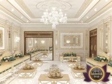 This is a picture of a luxury dining room with white walls and gold accents. The floor features a stunning white and grey marble tile, while the walls are decorated with gold leaf and intricate crown molding. The ceiling has beautiful crystal chandeliers and the walls have a luxe beaded wallpaper. A large, round dining table is set in the middle of the room, surrounded by luxurious high-backed chairs with cream upholstered cushions. On top of the table is a grand, flower-filled centerpiece that adds a touch of elegance and sophistication.