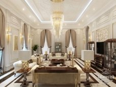 This picture shows an elegant, contemporary interior room design. It features white leather furniture with gold accents, a large abstract artwork on the wall, and a cream-colored marble floor. The room's soft lighting creates an inviting atmosphere, while the use of warm colors and luxurious textures adds to its sophisticated aesthetic.