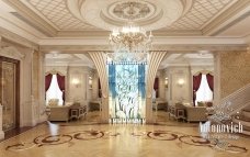 The picture shows a large, ornately decorated archway. It is made of white and gold marble, with intricate carvings in the curved, vertical frame. Decorative lamps are lined up along the top of the archway. The walls of the room are lined with mirrors and intricate tile work depicts a landscape-like scene.