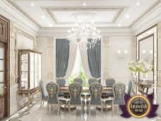 This picture shows a luxurious dining room with modern design elements. The walls are painted an elegant gray color, and the floor is covered with white marble tiles. A large wooden table with seating for six people is in the center of the room, and a white chandelier hangs from the ceiling. The walls also have a built-in cabinet with glass doors and shelves, and there is a colorful abstract painting on the wall.