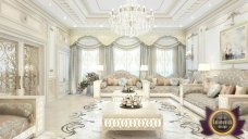 This picture shows a luxurious and modern entryway with white walls and a set of double glass doors. The floor is a beautiful marble tile and there is an intricate chandelier overhead. Along one wall, there is an arrangement of four large silver wall mirrors that reflect the light from the chandelier. There is also a large potted plant for decoration.