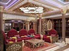 This picture shows a grand staircase in an ornate interior. The staircase is wide and spirals up around the inside of the room, lined with a marble handrail and luxurious carpets. The walls are painted a deep shade of blue and adorned with elegant gold fixtures. The near side of the room is decorated with a painting of a woman and various other lavish furniture pieces.