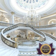 This picture shows a modern interior design displaying a grand double staircase with elaborate details. The staircase is decorated in white marble and gold accents, with a curved black banister flowing from the top to the bottom of the stairs. There are also two luxurious crystal chandeliers hanging from the ceiling above the stairs, adding an elegant touch to the space.