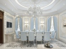 The picture shows a stunning living room with white and pale beige colors. The walls are painted in a light beige color, while the furniture is in a stark white. There is a large single-panel window in the center of the wall that provides plenty of natural light. The floor is composed of a chevron-style pattern of light and dark wood, in an intricate combination of colors. The seating includes two cream-colored sofas and one armchair, all upholstered in velvet. The rectangular coffee table has a white lacquer finish and is decorated with