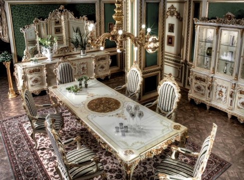 This picture shows a luxurious dining area designed with modern and traditional elements. The room has golden walls, a tufted white sofa, and a sleek glass-top table with ornate chairs. There is a patterned rug in the center of the room and large windows with open curtains. A large crystal chandelier hangs from the ceiling, adding a sense of grandeur.