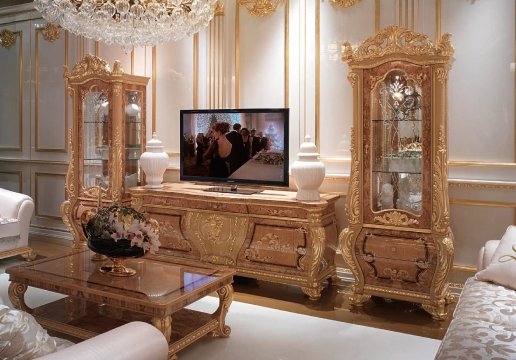 This picture shows a modern, contemporary living room. The walls are painted a light beige color and accented by built-in shelves and cabinetry in dark brown tones. The furniture is made up of two black leather couches, a glass center table, and a cowhide ottoman. There is an abstract painting hung on the wall above the fireplace and a few decorative pieces scattered around the room.