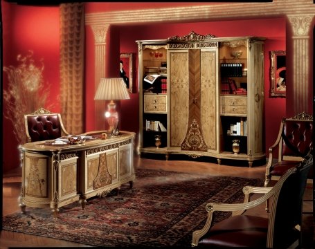 This picture shows a luxurious living room with an ornate light fixture and cream-colored walls. The furniture is decorated with patterned pillows and an area rug, while two armchairs can be seen in the foreground. An ornate mirror hangs over the fireplace, and several plants and accessories complete the look.