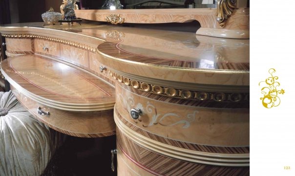 The picture depicts a small, wooden box with a large handle on top. The top of the box has a slanted lid with an intricate design of two birds and floral scrollwork. There is a brass latch at the front of the box and several decorative nails at the sides and corners. The box appears to be made of light-colored wood and has a slightly aged or weathered look.