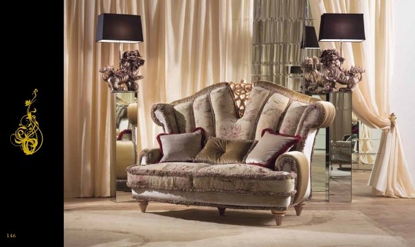 This picture shows a contemporary living room with elegant and luxurious furniture. The walls, ceiling, and floor all have a light-colored finish and are accented by dark wood molding. The centerpiece of the room is a large leather sofa with plush cushions, which sits atop a white shag rug. On either side of the sofa are two stylish armchairs upholstered in a modern turquoise fabric. A glass and metal coffee table sits between the chairs, providing the perfect place to rest drinks or snacks. There is a modern fireplace on one wall, as well as shel