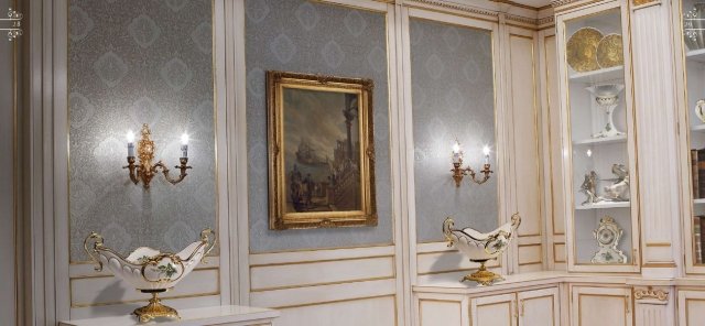 This picture shows a luxurious bathroom with a modern design. The main feature of the room is an elegant soaking tub which is set in the center of the space on a marble platform with steps. There are also two white vessel sinks with chrome faucets on either side of the tub, as well as a large vanity with a black marble top and storage drawers. The walls and floors have a light wooden finish, and there is a large window with white shutters for natural light. The overall look is modern and sophisticated.