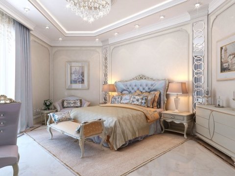 This picture shows a luxurious bedroom interior with a beige and ivory color scheme. The room is decorated with a large, ornate bed surrounded by velvet drapery and embossed wallpaper. On either side of the bed are glass side tables filled with decorative items. The floors have white marble tiles and the walls feature wall sconces and framed art. There is also an intricately carved mirror and a chaise lounge at the end of the bed.