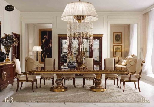 This picture shows a modern living room with contemporary furniture and decorations. The room is decorated in shades of white, with walnut hardwood floors and a leather sofa in the center. The walls are painted white and the ceiling is open beam with exposed woodwork. There is a large wall-mounted television in one corner, and two artistic abstract paintings hanging on either side of it. A coffee table and two armchairs are also present, along with various house plants and a few small decorative elements scattered around.