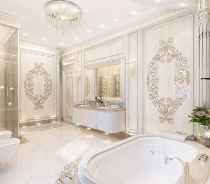 This picture shows a white marble kitchen with a large central island and a beautiful range hood above it. The kitchen has multiple built-in cabinets, dark granite countertops, and stainless steel appliances. There is a large sink in the island, and the walls and floor are tiled in light gray marble.