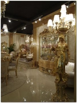 This picture shows a spiral staircase in an elegant entryway. The staircase is made of a dark metal and features intricate designs on the railing. The walls are decorated with various art pieces and there is a light fixture at the top of the stairs that provides the room with a warm glow.