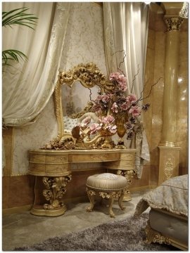 This picture shows a luxurious bathroom with a freestanding bathtub. The tub is white and has gold detailing around the top and bottom edges. The walls are a light grey and are decorated with elegant gold tiles. The floor is also a light grey with black accent tiles near the center. There is a large window in the background looking out onto a cityscape. The room also contains two vanities with stone sinks, one on either side of the tub, and two separate shower stalls with glass panels.